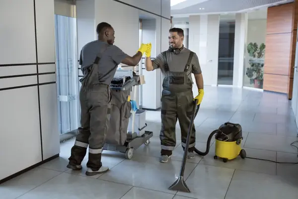Equipe de limpeza uniformizada com carrinho e aspirador em corredor comercial